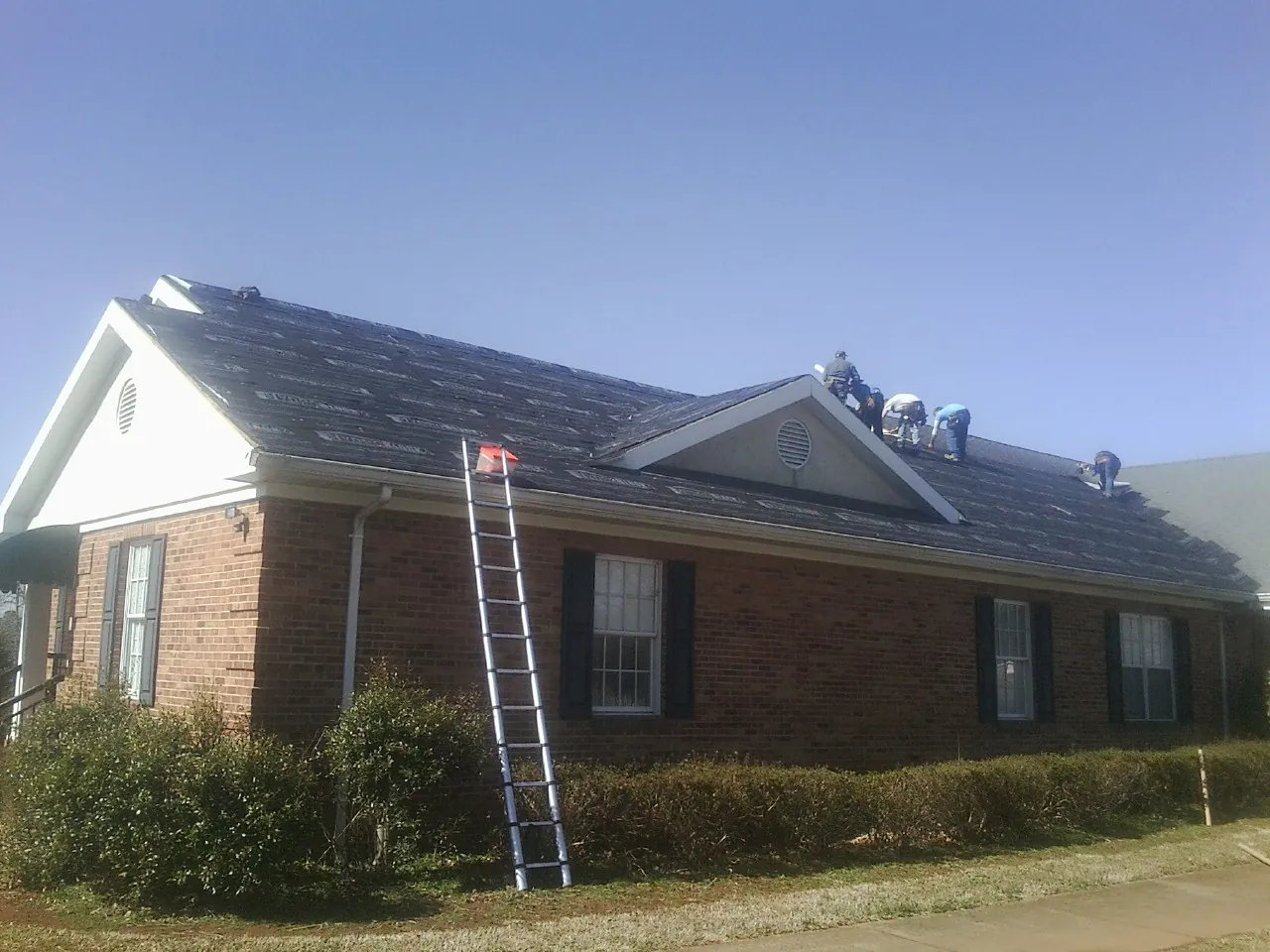 Crew tearing shingles off a brick ranch roof with a ladder set — Metal Roof Repair work by our crew in Saint Clair