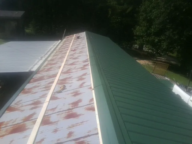 Old rusted panels beside newly installed green metal roofing — Wind Damage Roof Repair by Roofing Brothers in Saint Clair