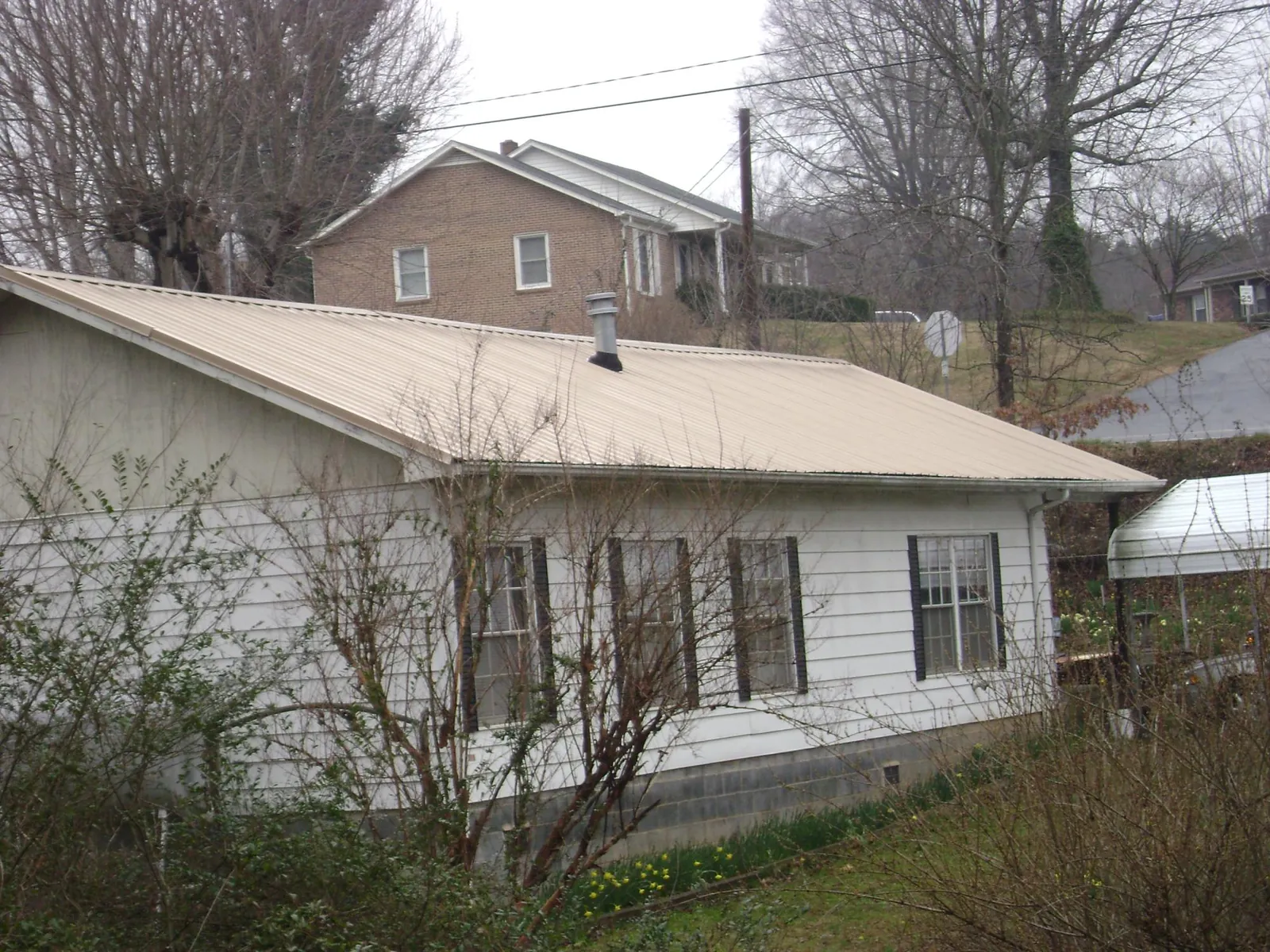 Tan metal roof on a white sided house set into a hillside — Commercial Roofing by Roofing Brothers in Saint Clair