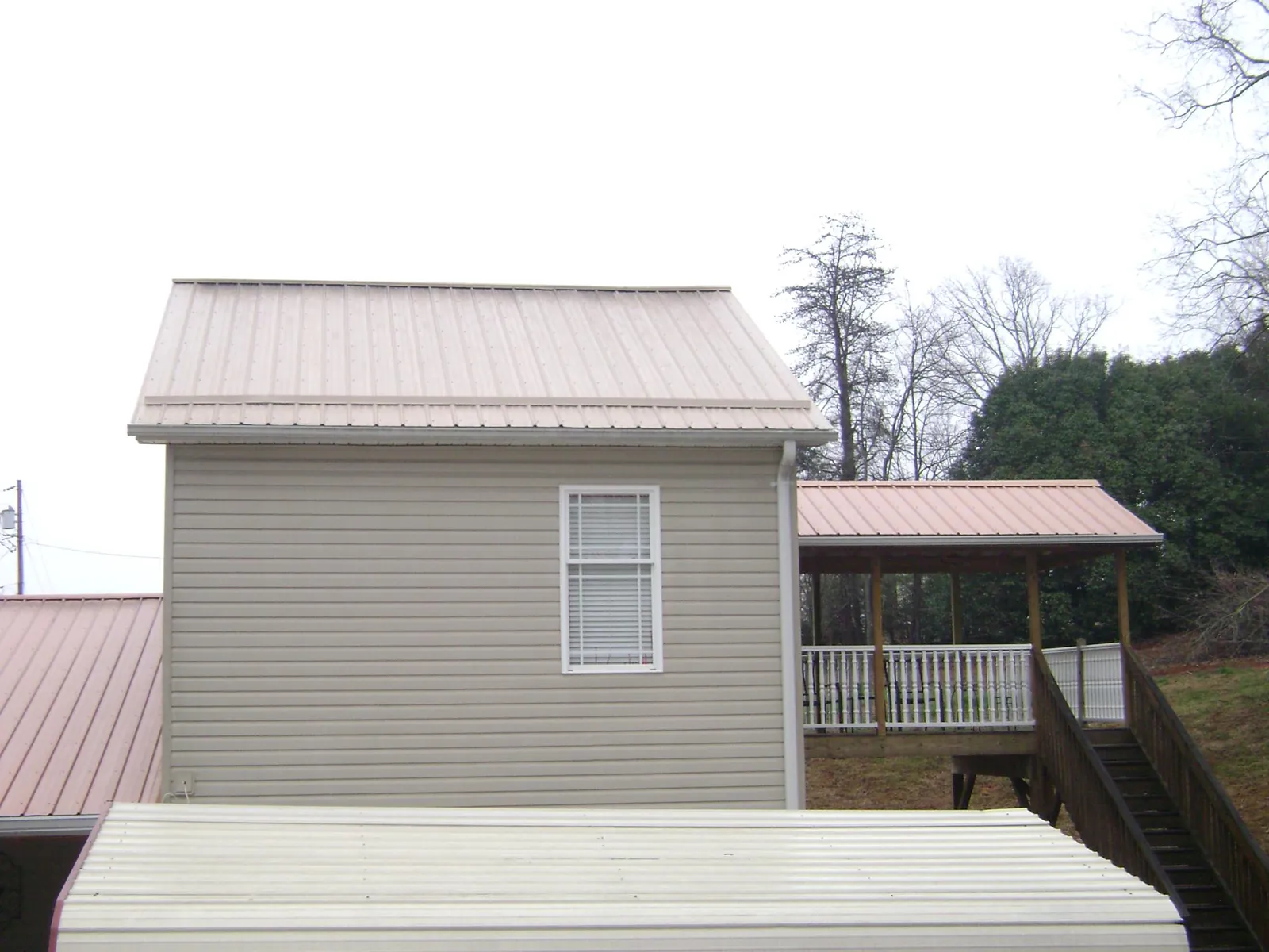 Tan metal roofs on a two story addition and attached porch, from a Roof Replacement job in Saint Clair